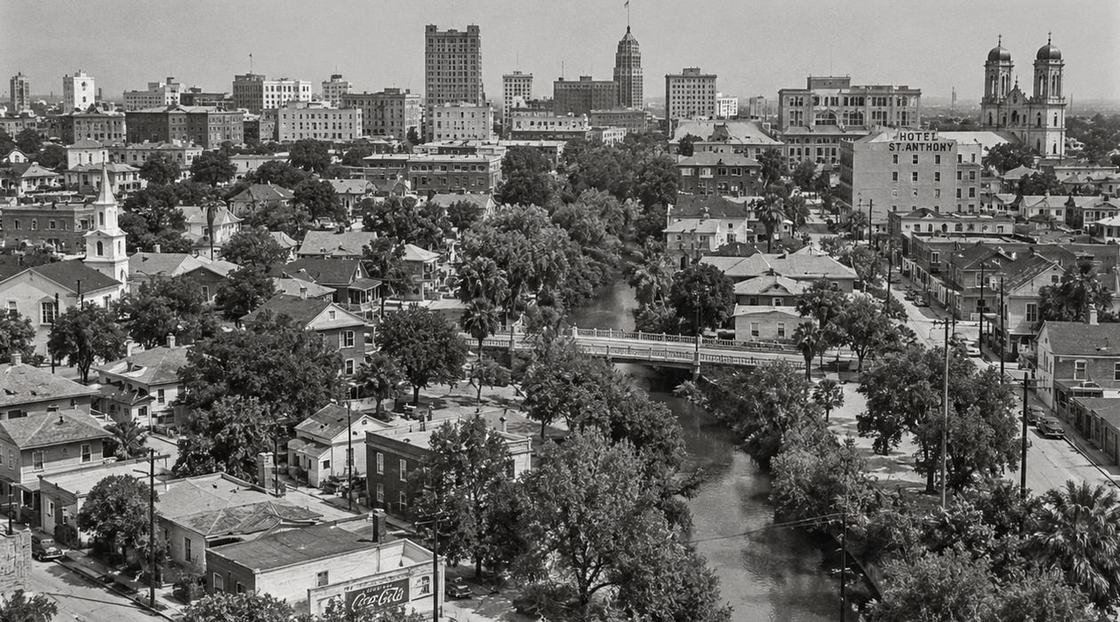 Illustrated reconstruction: Black and white view over Germantown toward downtown: houses, trees, a church steeple, Hotel St. Anthony and the river bridge.